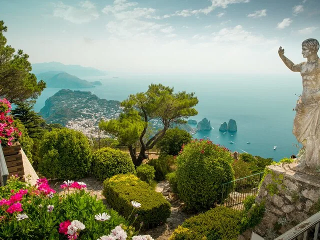 Scenic view overlooking the coast with a statue and lush gardens.