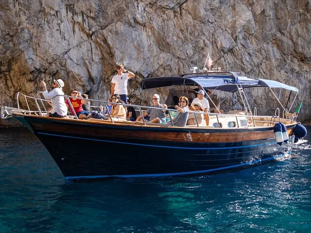Group of tourists enjoying a boat tour near a rocky cliff.