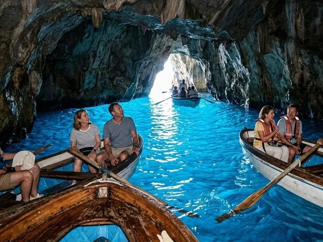 Tourists in rowboats exploring a sea cave with bright blue water.