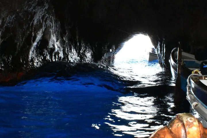 Inside a sea cave with glowing blue water and an entrance opening.
