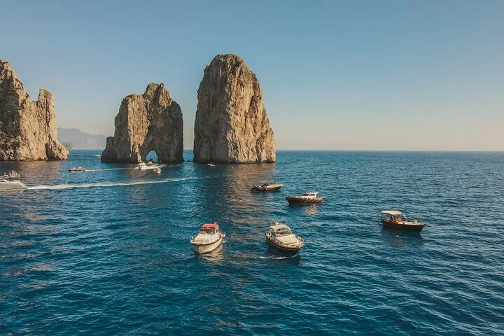 Several boats cruising on the sea near the famous Faraglioni rocks.