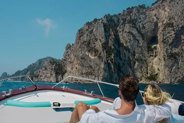 Couple relaxing on a boat looking towards the rocky coastline of Capri.
